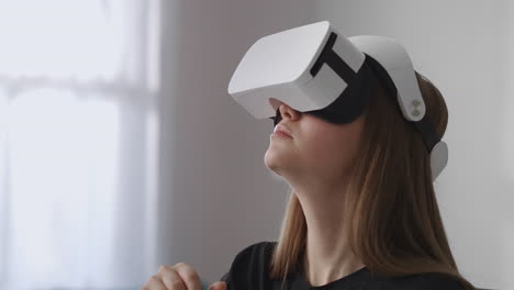 female-user-is-using-new-head-mounted-display-for-playing-games-sitting-in-living-room-and-moving-hands-for-controlling-modern-technology